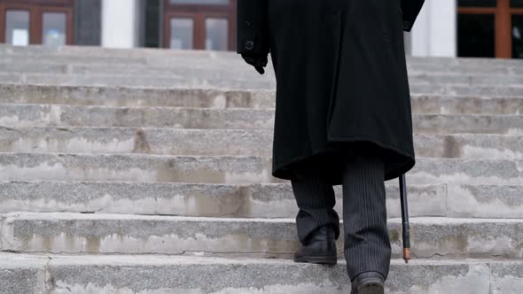 An Old Grandfather in a Black Coat Climbs the Stairs Walking Hard alt