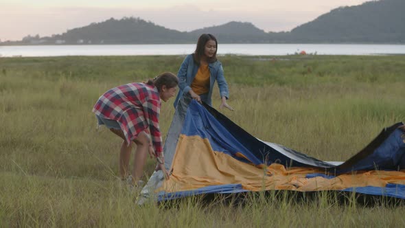 Group of a young Asian women camping pitch a tent enjoying having fun together a summer traveling.