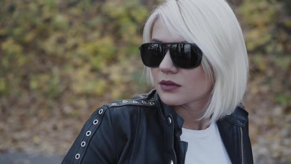 Portrait of Stylish Blonde in Sunglasses and Leather Looking Aside alt
