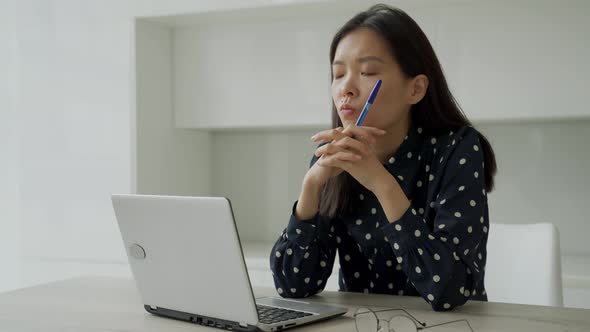 Thoughtful Young Business Asian Woman Holds a Pen and Looks Out the Window While Working with a alt