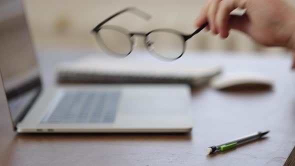 Glasses lie near the laptop at the workplace on a blurred background. alt