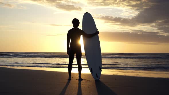 Surfer looking out at ocean as sun rises in the distance