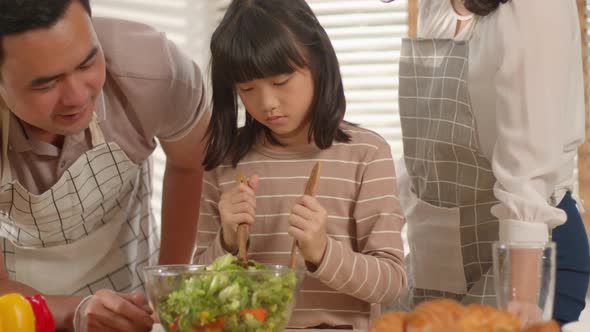 Family Mother, Father, and Cute Little Girl cooking salad spending time together in the kitchen.