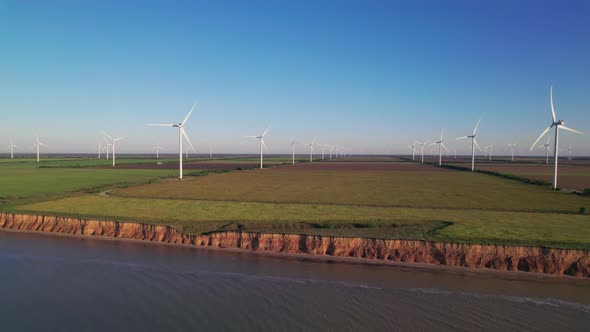 Windmills on a cliff above the sea, top view. Wind farm with turbine cables for wind energy.