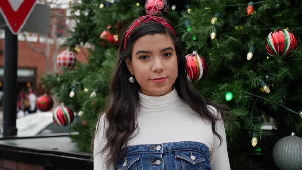 Young woman out Christmas shopping in the city with a tree decorated with ornaments and festive holi alt