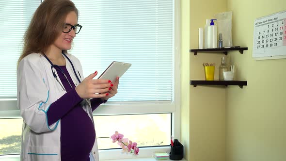 Pregnant Female Doctor Using Tablet Computer at Work and Smile Looking at Camera
