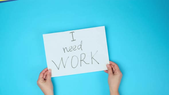 two female hands hold a white sheet of paper with the inscription I need work alt