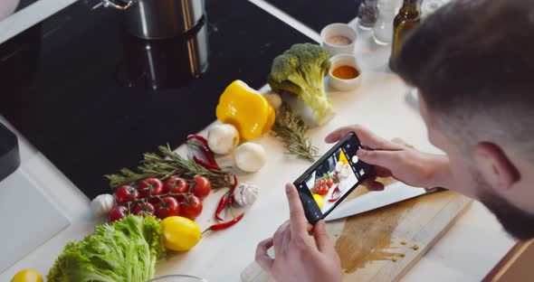 Close Up of Young Man Cooking and Taking Photos on Smartphone in Kitchen alt