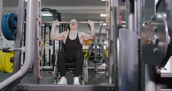 A wheelchair user performs strength exercises in the Smith machine in the gym.