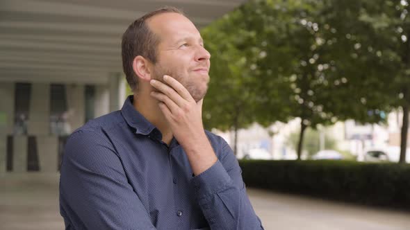 A Caucasian Man Thinks About Something By an Office Building in an Urban Area  Closeup