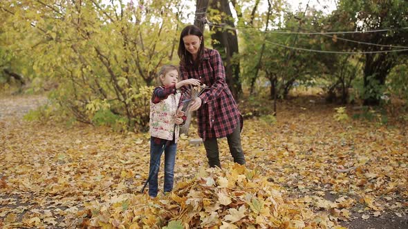 Little Girl Helps Mom Clean Yellow Leaves in the Yard with a Rake