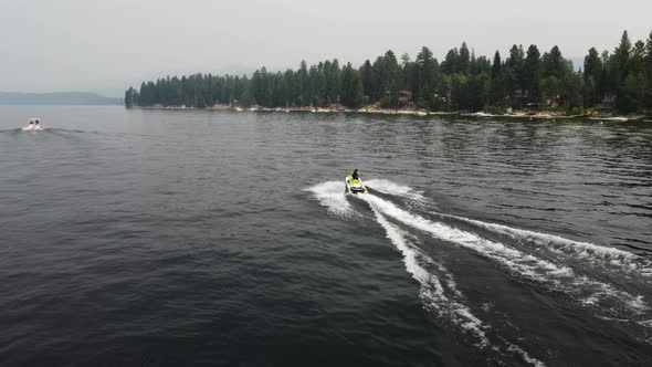 Drone shot following a person driving a jet ski at Payette Lake in McCall, Idaho with the shore and alt