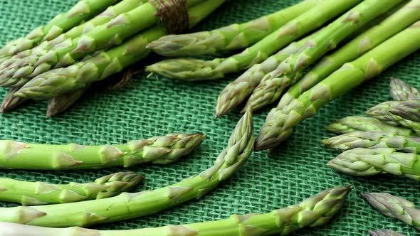 Raw garden asparagus stems. Fresh green spring vegetables on green jute background.