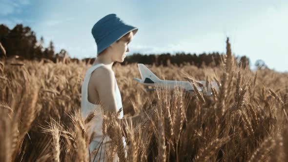 Cinematic Boy in a Hat Playing with Airplane in the Golden Wheat Field Moving Camera