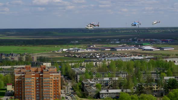Group of Three Helicopters Fly One After Another to Suburbs with Houses and Green Fields on Sunny