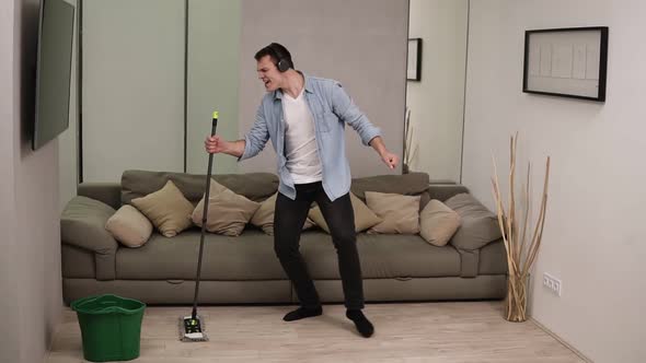 People Housework and Housekeeping Concept Happy Man in Headphones with Mop Cleaning Floor and alt