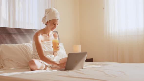 Young Girl with Long Hair in White Robe Using Laptop Having Breakfast Orange alt
