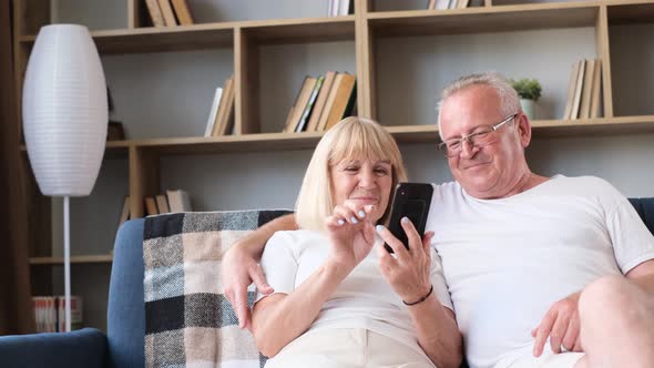Happy Senior European Pensioner Couple Holding Smartphone Laughing Looking at Funny Photos alt