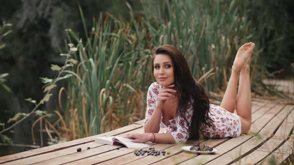 Woman Reading a Book Lying on a Wooden Pier By the Lake alt