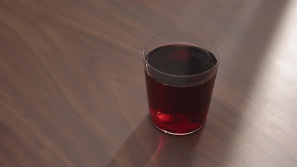 Slow Motion Handheld Shot of Red Drink in Tumbler Glass on Walnut Table with Copy Space