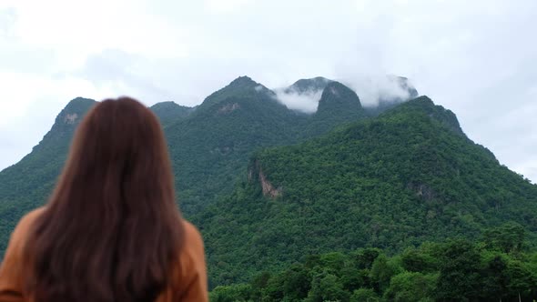 Rear view of a female traveler looking at a beautiful mountains view on foggy day