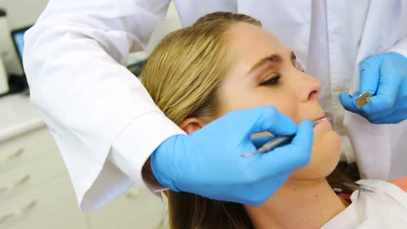 Dentists examining a female patient with tools alt