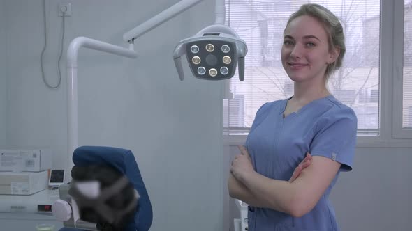 Portrait of Pretty Smiling Female Dentist Assistant Near Dental Chair in Clinic alt