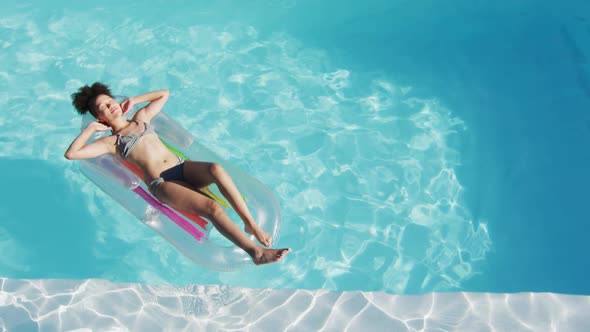 Mixed race woman having fun sunbathing on inflatable in swimming pool alt