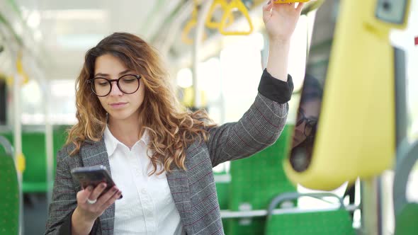 young caucasian business woman rides in public transport standing inside a bus.  alt
