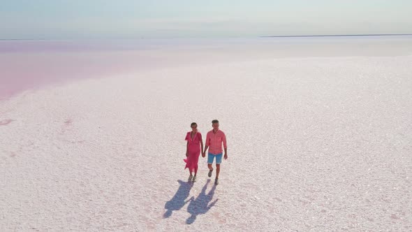 Aerial Epic Drone Image of Lovely Romantic Couple Walking Along Bright Colorful Pink Water of alt
