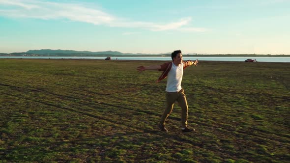 slow-motion of cheerful man running with arms raised across the green field with sunlight