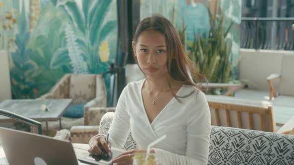 A Young Asian Girl Works at Her Laptop in a Rooftop Cafe in the City alt