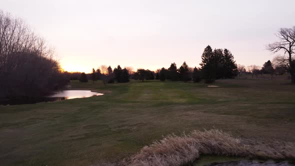 Tracking shot moving forward over golf course during sunrise. Flag flapping in the wind as drone fly alt