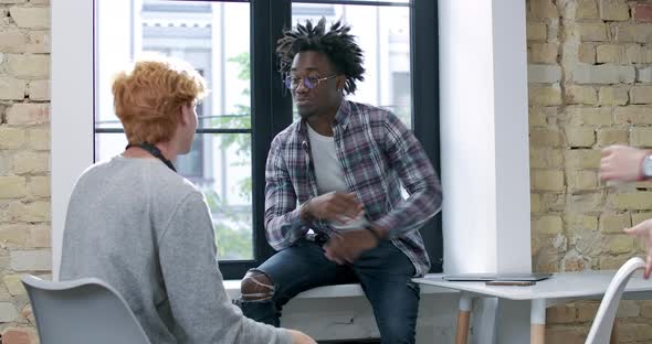Relaxed Caucasian and African American Men Chatting During Break in Office. Cheerful Young Woman alt