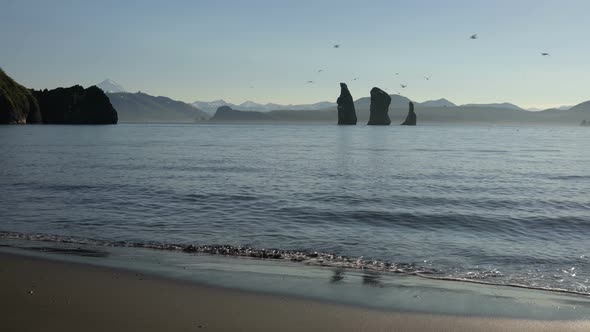 Rocky Islands in Sea and Beach of Black Volcanic Sand on Sunny Day