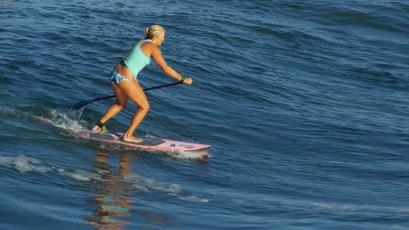A young woman SUP surfing in a bikini on a stand-up paddleboard surfboard. alt
