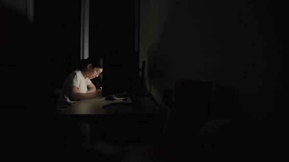 A young woman writes an article on a tablet at night in a home office.