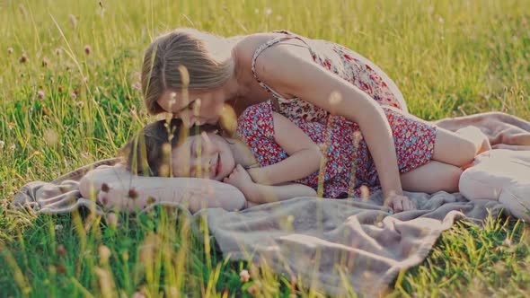 Young Charming Mother in a Summer Dress Tenderly Kisses and Hugs a Cute Little Daughter
