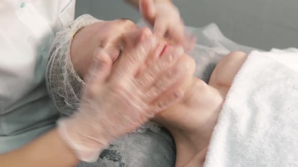 The Cosmetologist Applies a Gel to the Face and Does a Facial Massage