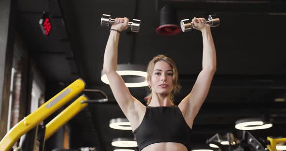 Portrait of Young Beautiful Athletic Woman Doing Biceps Exercises in the Gym Using Dumbbells