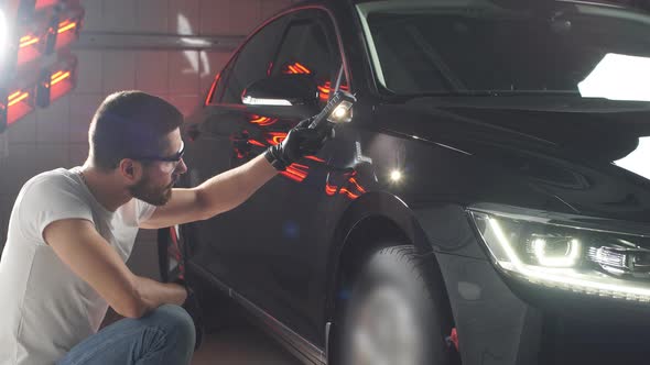 Man Checks Result of Polishing of Car with a Flashlight.