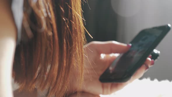 Young Woman Sitting on the Bed and Makes Online Shopping on a Smartphone. Online Shopping Concept. alt