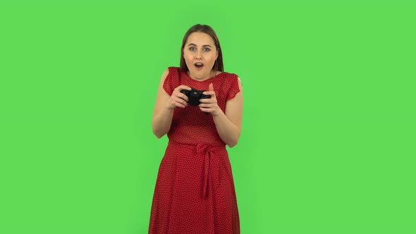 Tender Girl in Red Dress Is Playing a Video Game Using a Wireless Controller and Loses. Green Screen alt