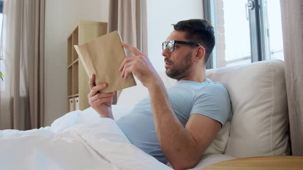 Man in Glasses Reading Book in Bed at Home