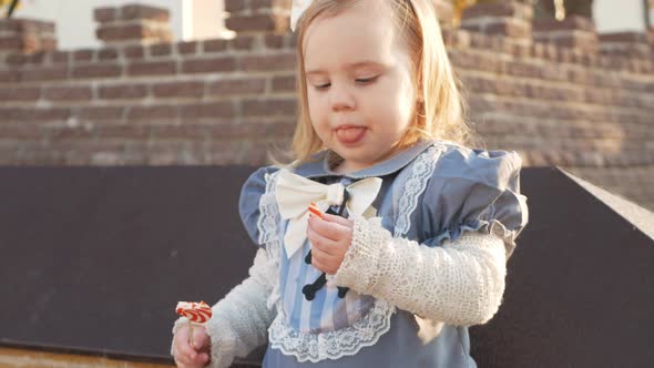 Little Girl Eats Delicious Candy in Witch Costume Orange Lollipop on Stick on October 31 Happy