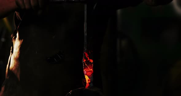 Mid-section of blacksmith holding forged iron rod alt