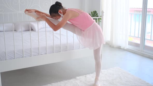 Asian ballet girl with pink dress and hygiene mask raise leg on bed before practice the dancing alt
