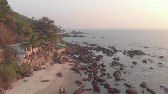Rocky ocean coast and old buildings in Arambol Beach at sunset in Goa, India - Aerial Fly-over shot alt
