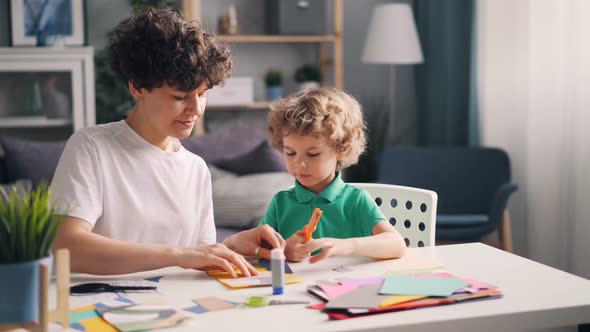 Mother and Son Busy Creating Colorful Paper Collage Sitting at Table at Home alt