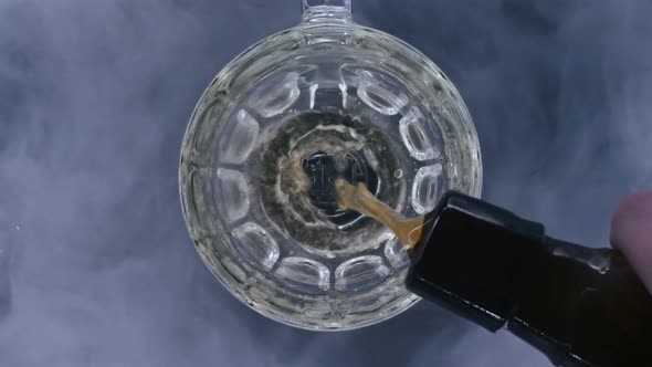 Top Close Up View of Beer Is Pouring From the Bottle Into Glass with Cold Smoke in Background in